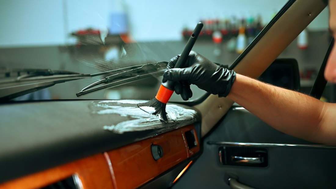 Detailer cleaning a car dashboard with a soft detailing brush