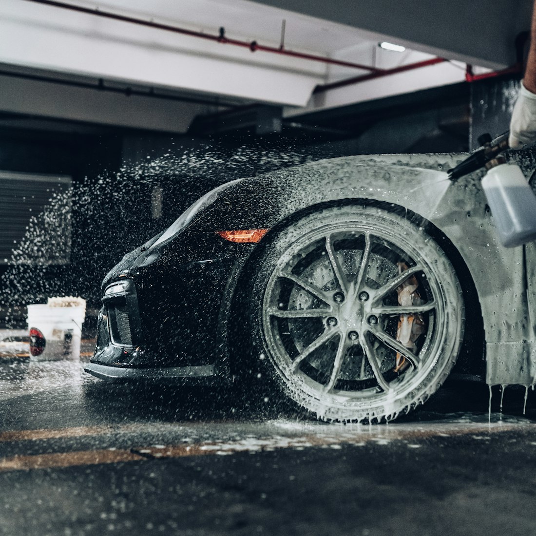 Foam cannon spraying a black sports car in a detailing garage