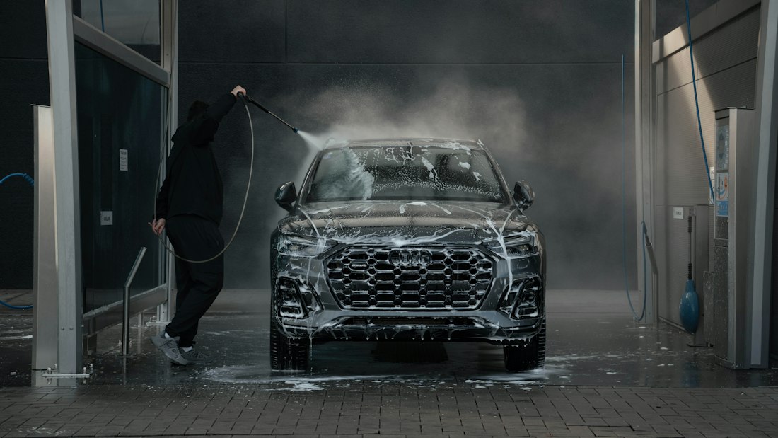 Technician hand washing a black car exterior with soap and water
