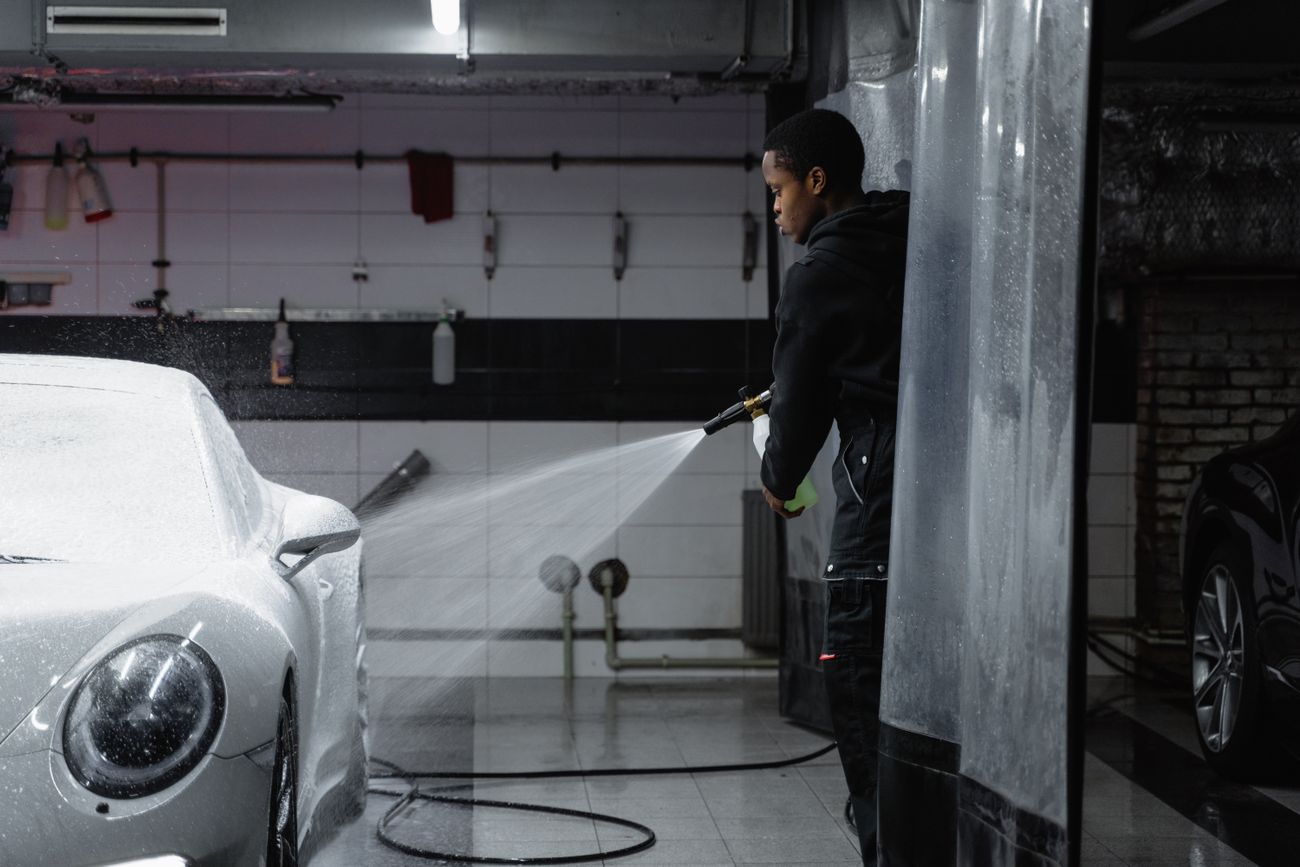 Technician using a pressure washer on a car in an indoor bay