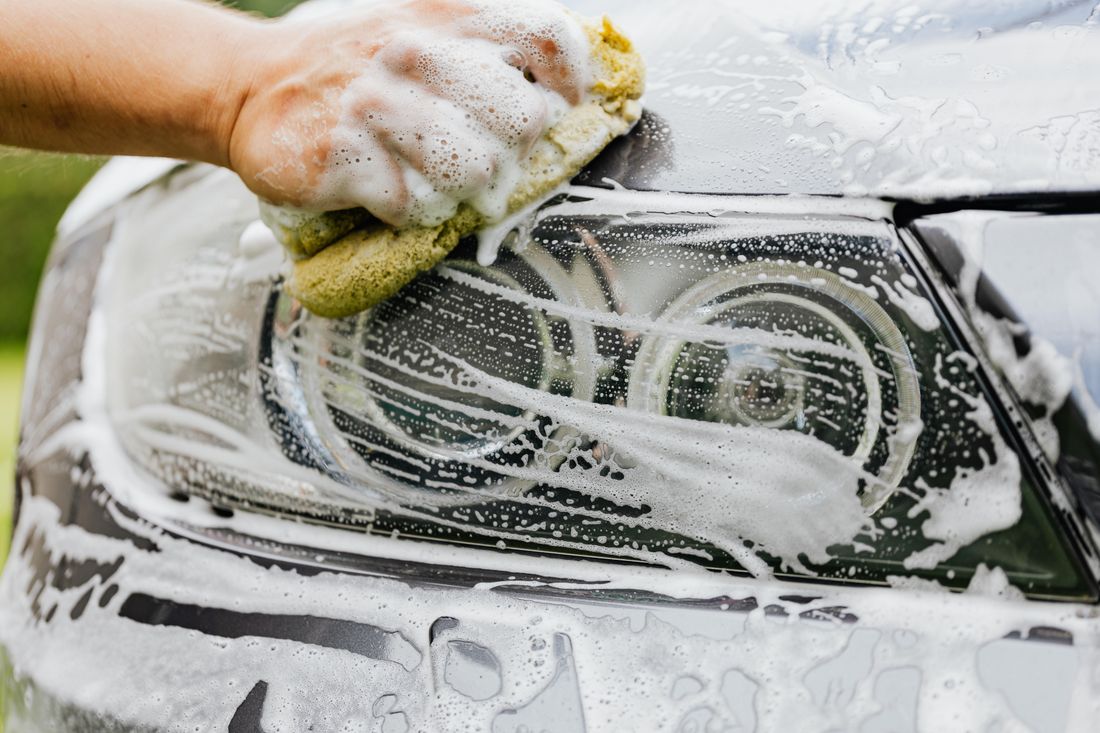 Hand scrubbing a car headlight with a soapy sponge