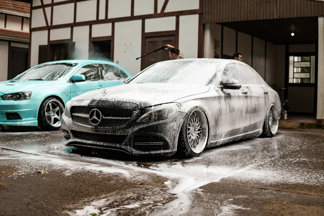 Two cars covered in foam inside a wash bay